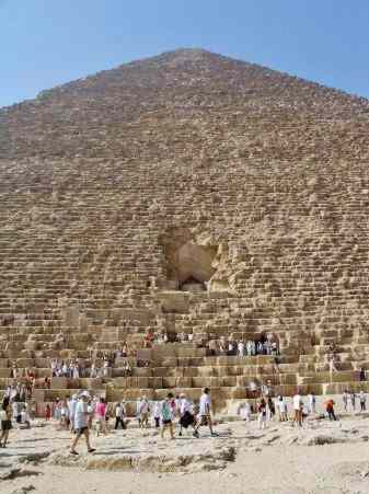 A line of tourists wait to enter the pyramid, while the true entrance stands above, unused.